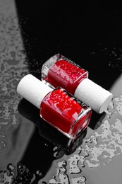 Photo of Nail polishes in bottles on wet dark surface