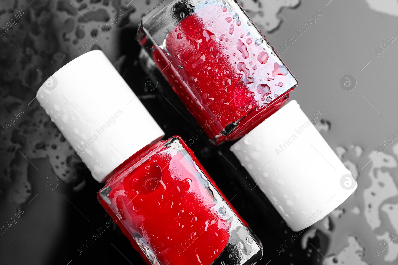 Photo of Nail polishes in bottles on wet dark surface, flat lay