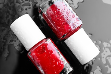 Photo of Nail polishes in bottles on wet dark surface, flat lay