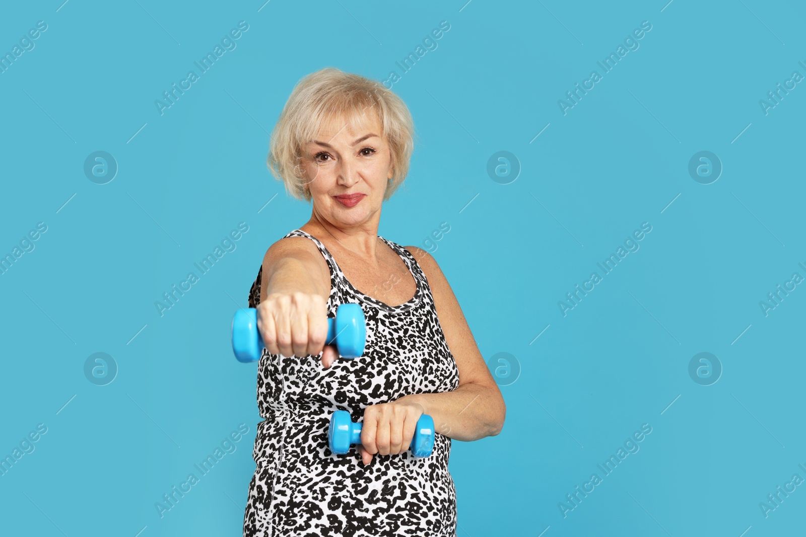 Photo of Senior woman exercising with dumbbells on light blue background, space for text