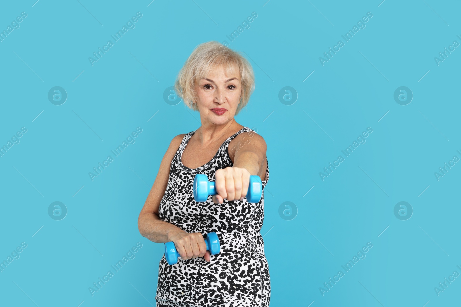 Photo of Senior woman exercising with dumbbells on light blue background, space for text