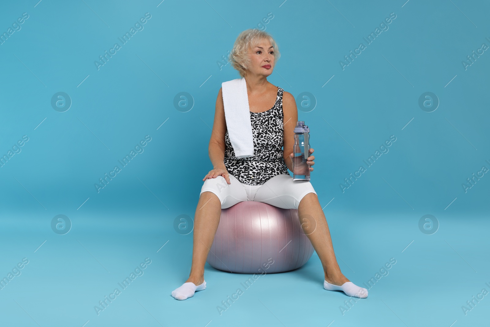 Photo of Senior woman with fitness ball, towel and water on light blue background