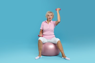 Photo of Senior woman exercising with fitness ball and dumbbells on light blue background