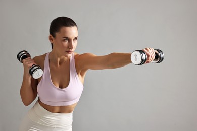 Photo of Woman in gym clothes exercising with dumbbells on grey background