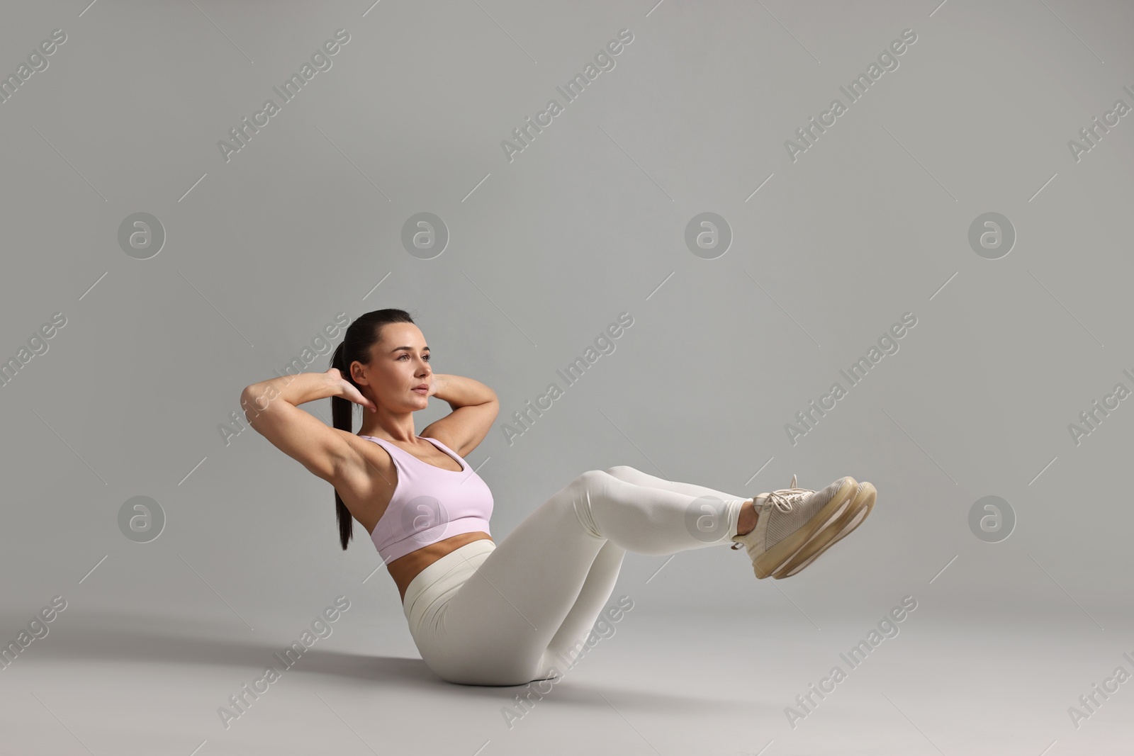 Photo of Woman in gym clothes doing abs exercise on grey background