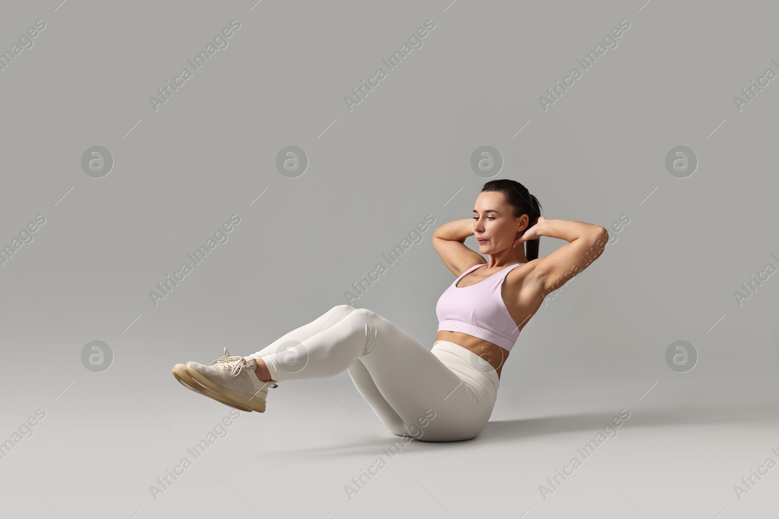 Photo of Woman in gym clothes doing abs exercise on grey background