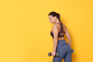 Photo of Beautiful woman with dumbbells training on yellow background. Space for text