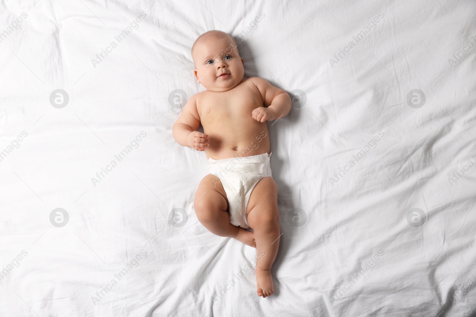 Photo of Cute little baby in diaper on bed, top view