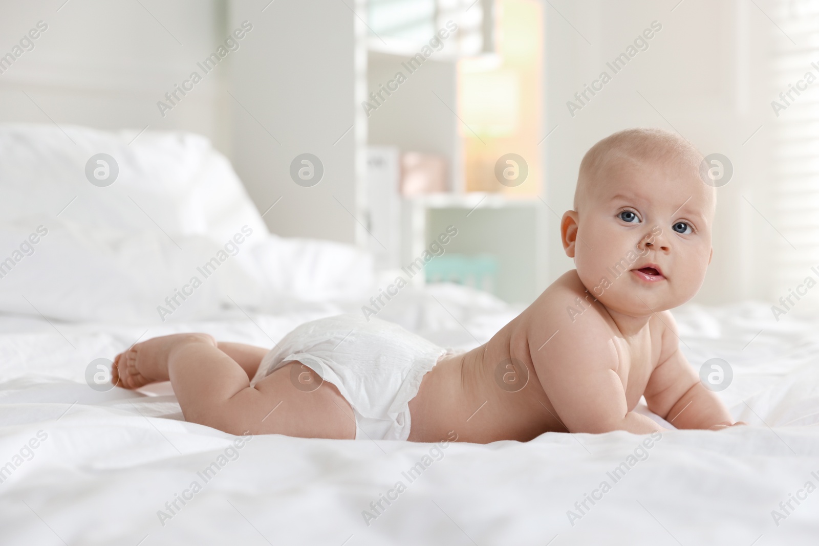 Photo of Cute little baby in diaper on bed indoors