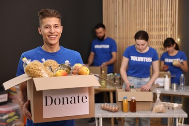 Photo of Volunteer holding donation box with food products indoors, selective focus