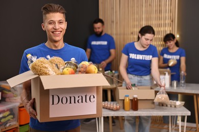 Photo of Volunteer holding donation box with food products indoors, selective focus