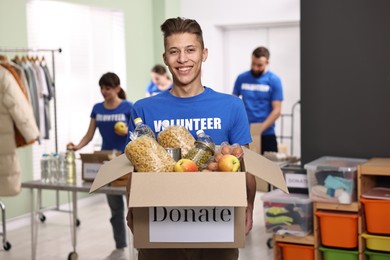 Photo of Volunteer holding donation box with food products indoors, selective focus