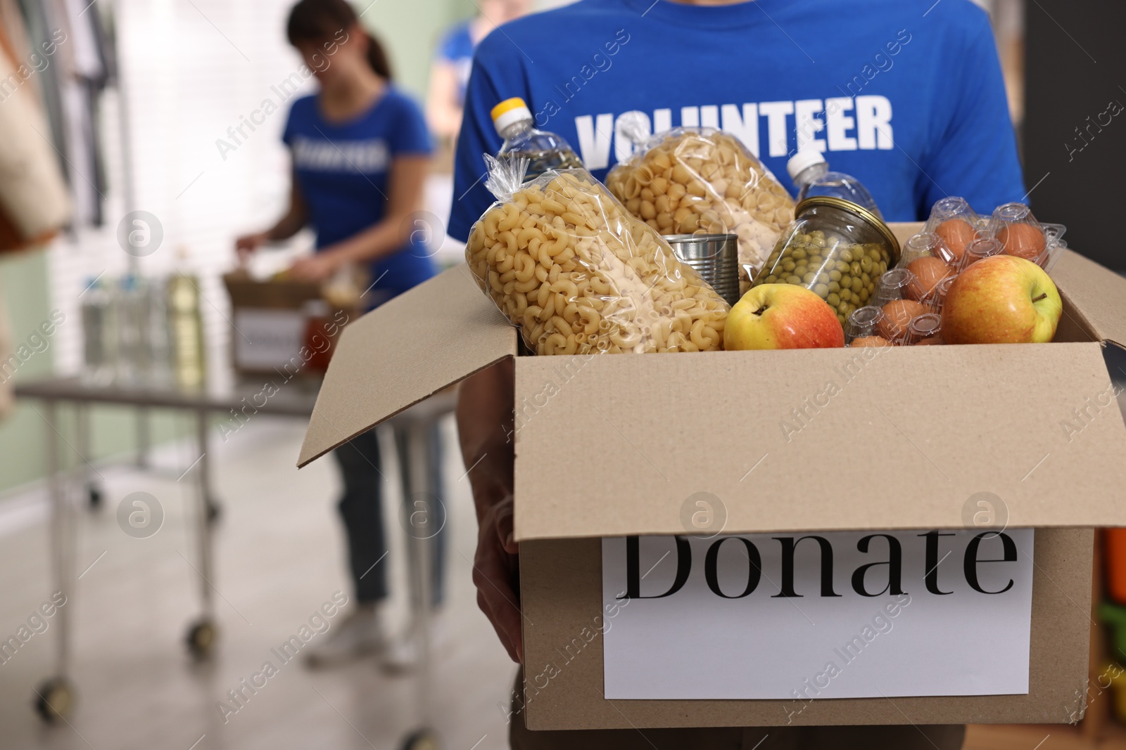 Photo of Volunteer holding donation box with food products indoors, closeup