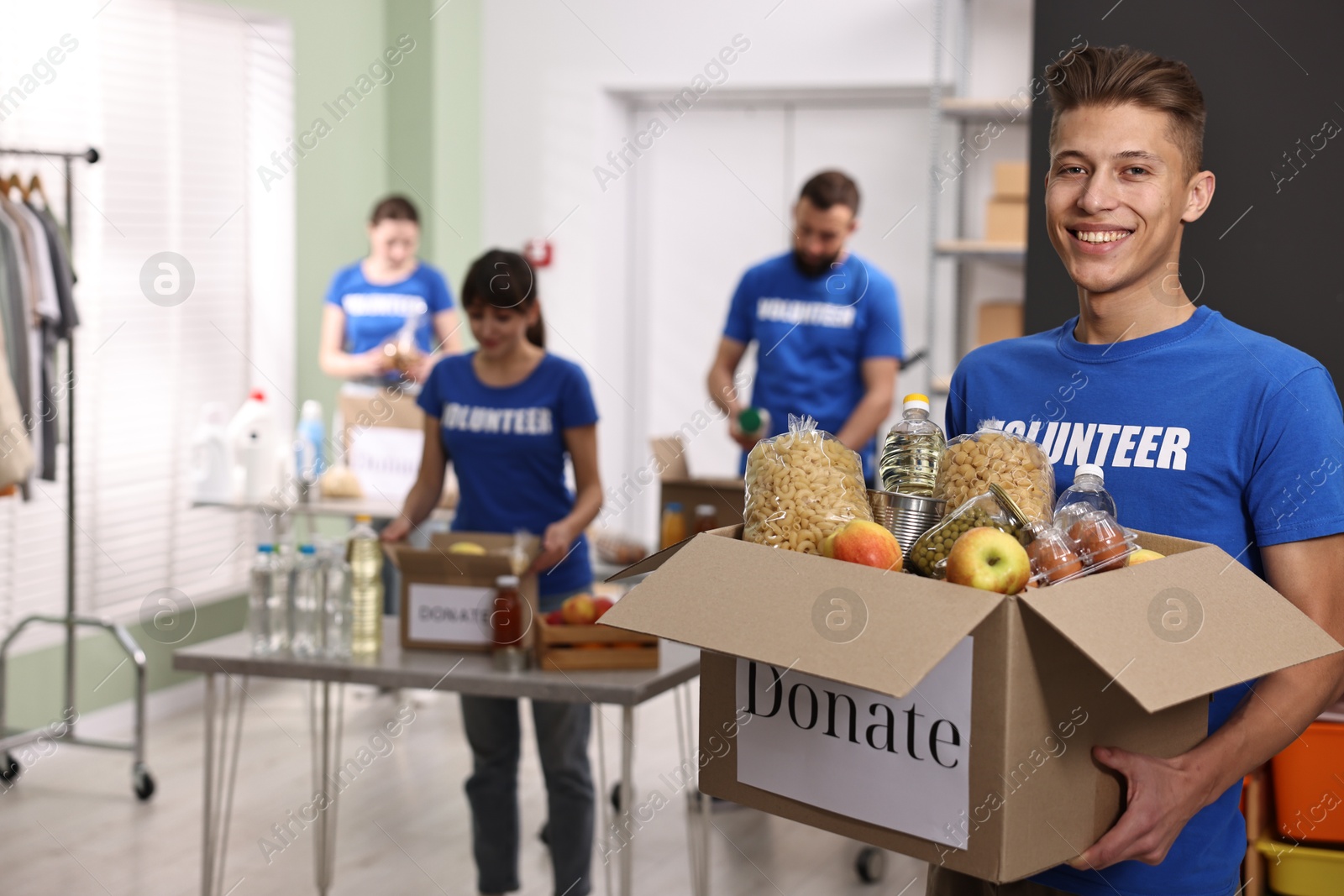 Photo of Volunteer holding donation box with food products indoors, selective focus