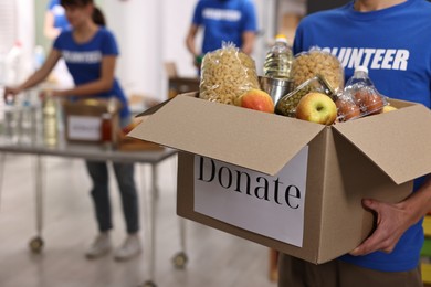 Photo of Volunteer holding donation box with food products indoors, closeup. Space for text