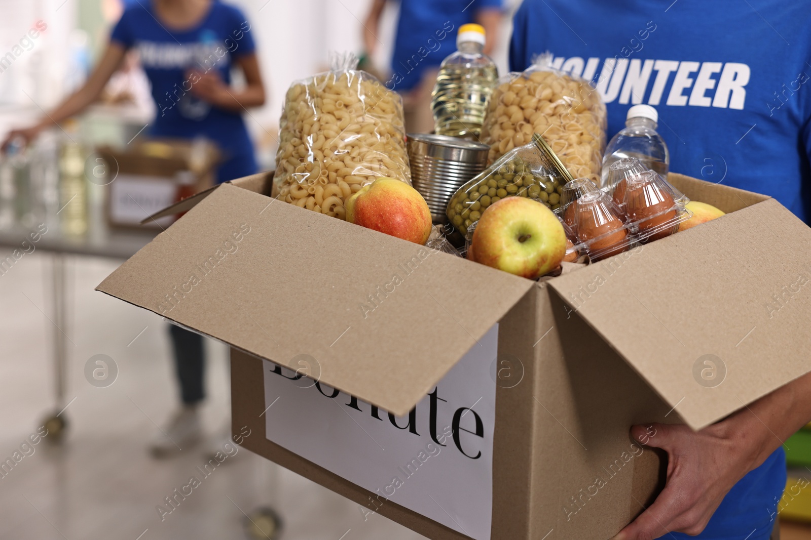 Photo of Volunteer holding donation box with food products indoors, closeup