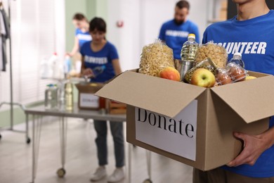 Photo of Volunteer holding donation box with food products indoors, closeup