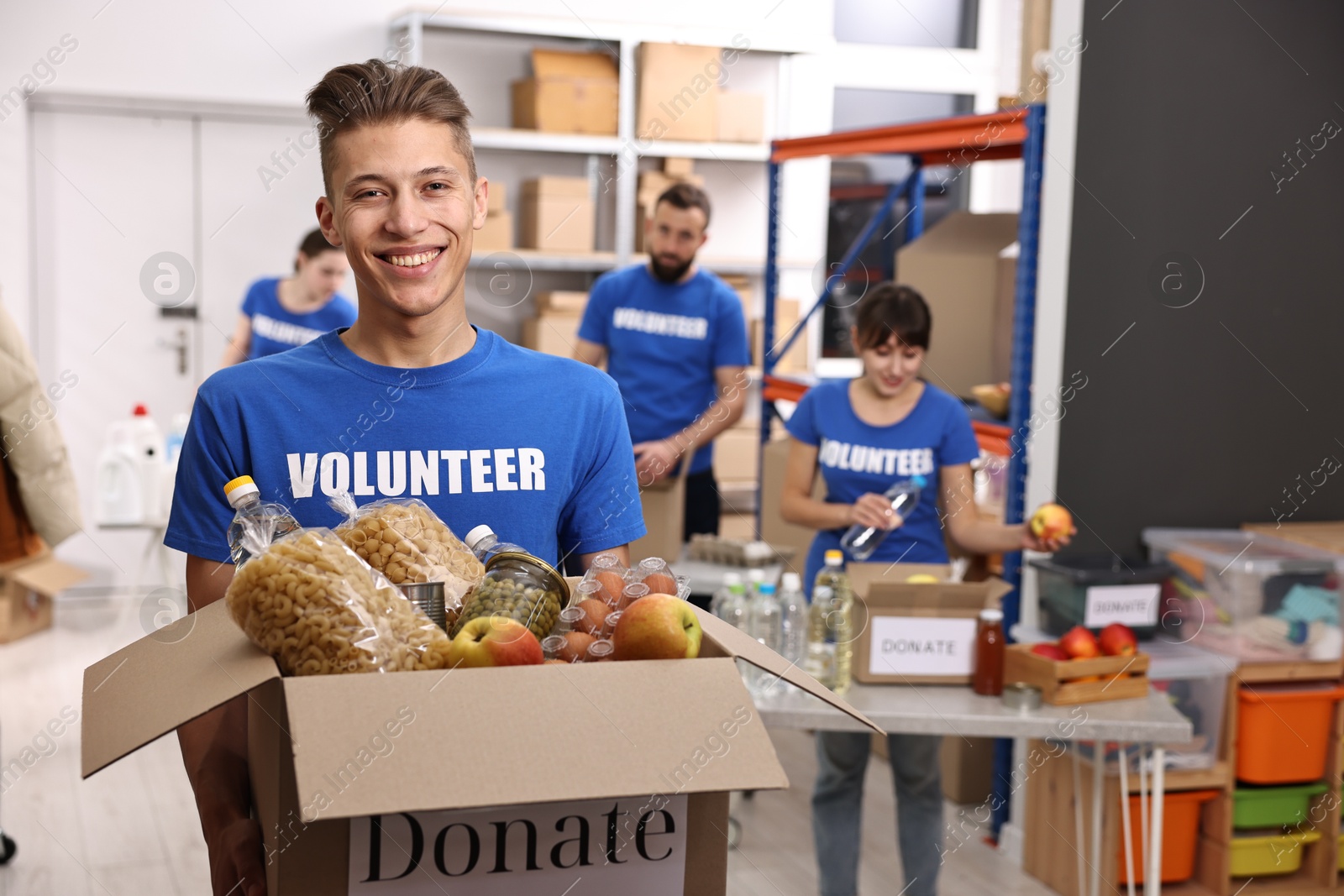 Photo of Volunteer holding donation box with food products indoors, selective focus