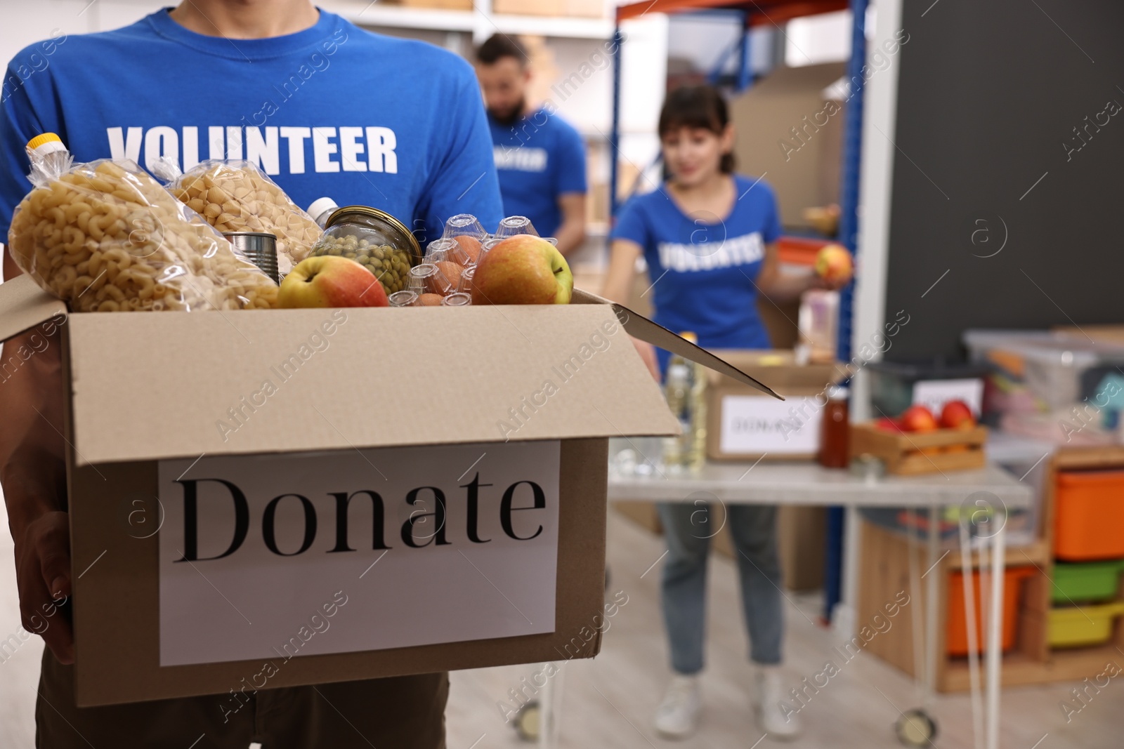 Photo of Volunteer holding donation box with food products indoors, closeup