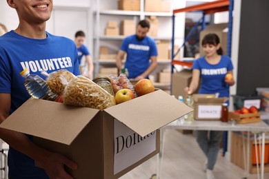 Photo of Volunteer holding donation box with food products indoors, closeup