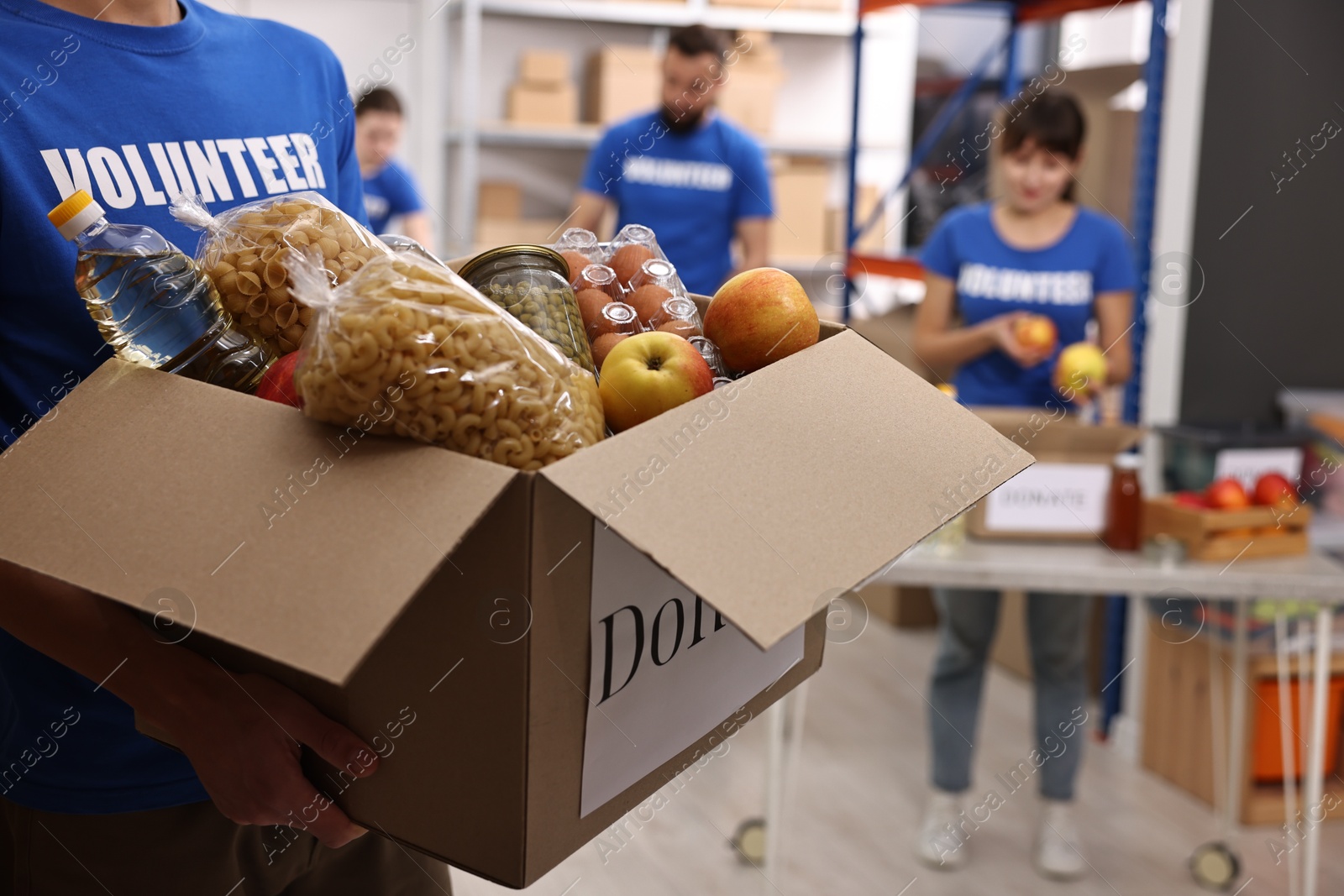 Photo of Volunteer holding donation box with food products indoors, closeup