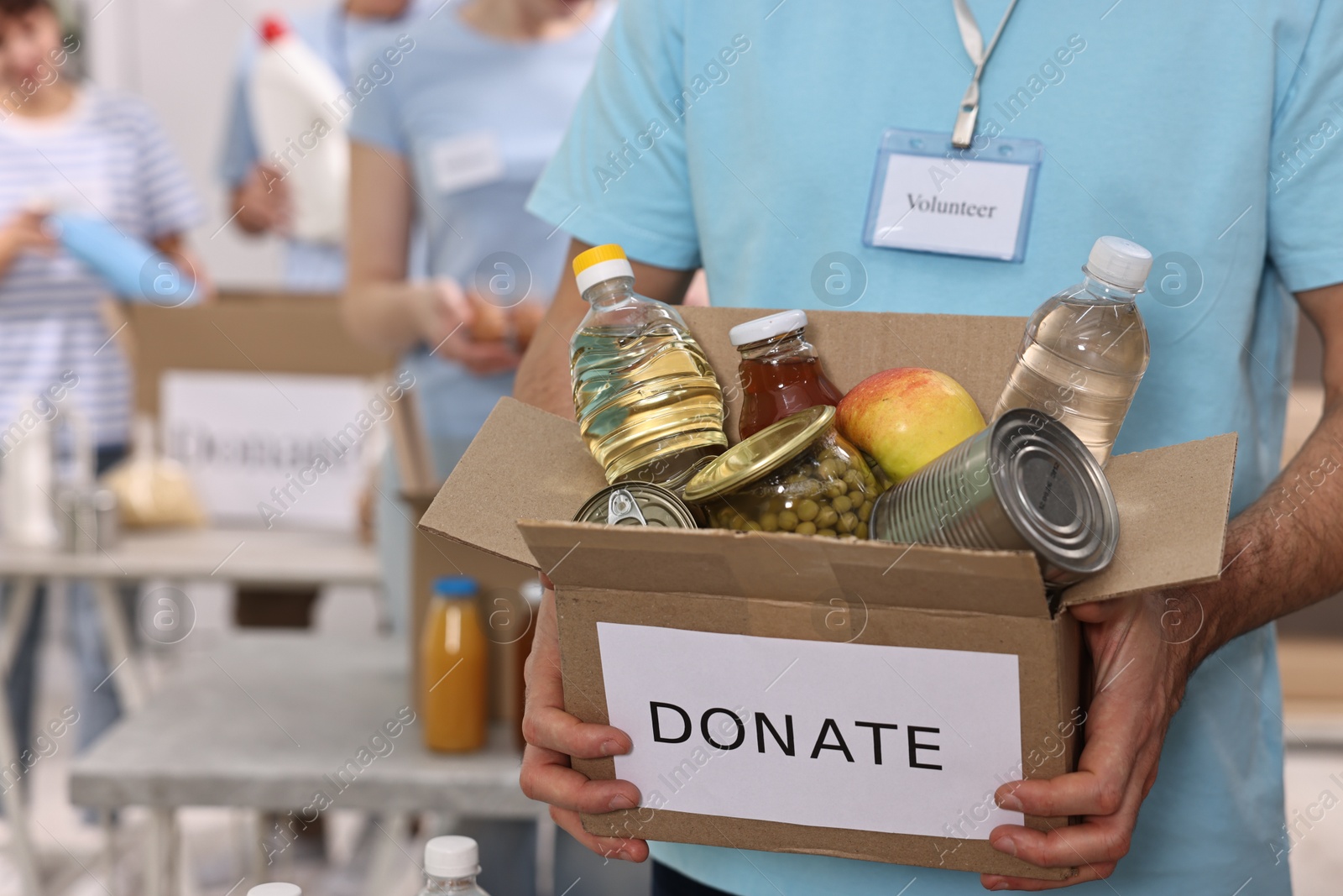 Photo of Volunteer holding donation box with food products indoors, closeup. Space for text