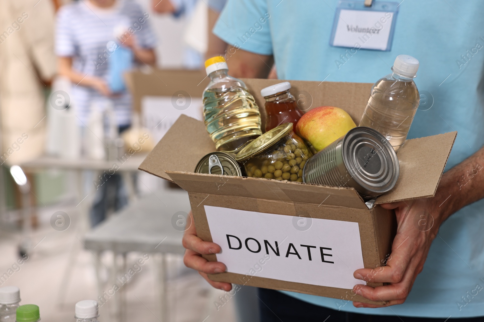 Photo of Volunteer holding donation box with food products indoors, closeup. Space for text