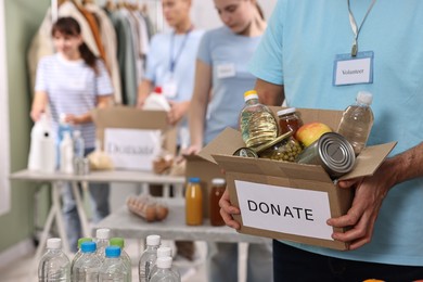 Photo of Volunteer holding donation box with food products indoors, closeup