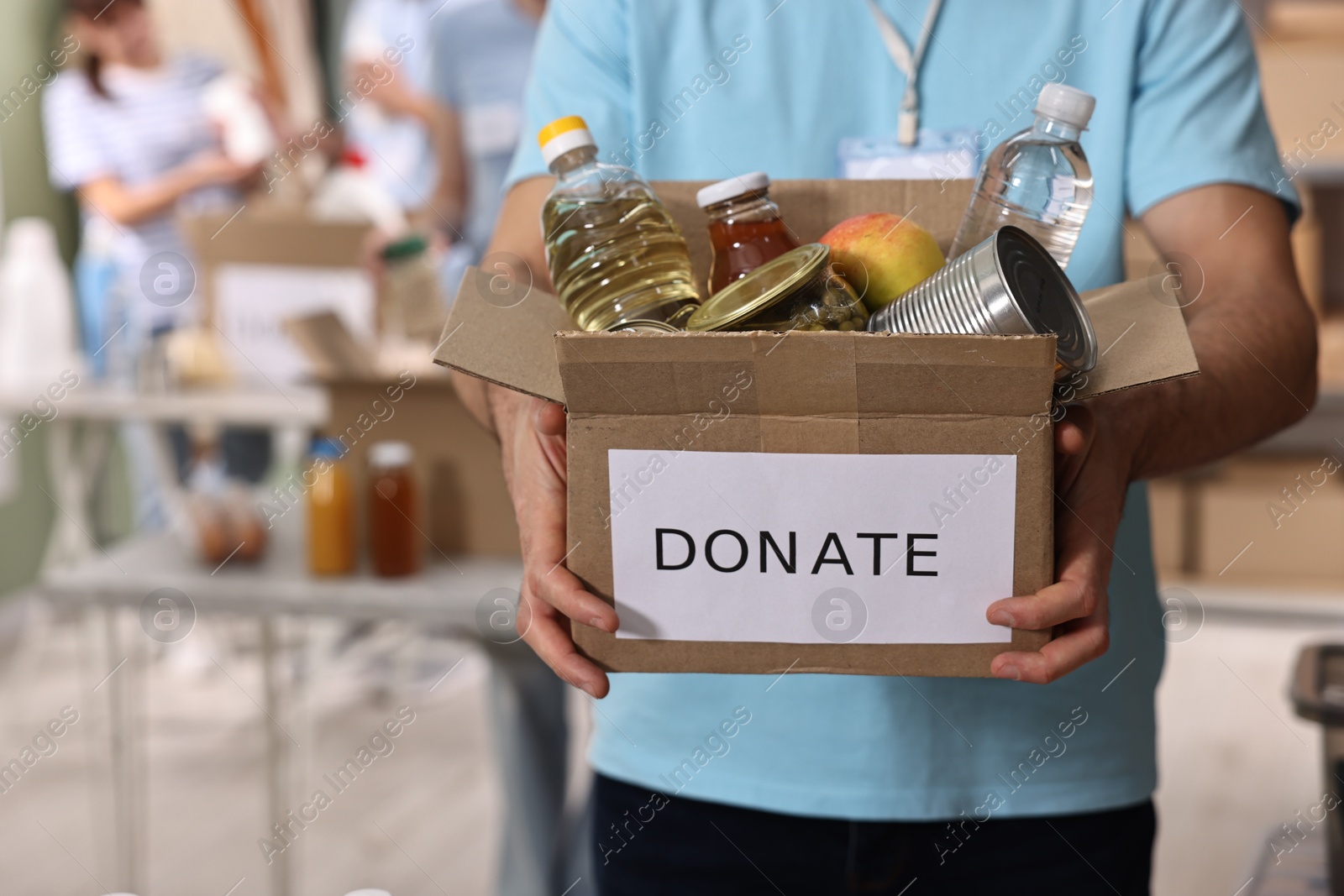 Photo of Volunteer holding donation box with food products indoors, closeup. Space for text