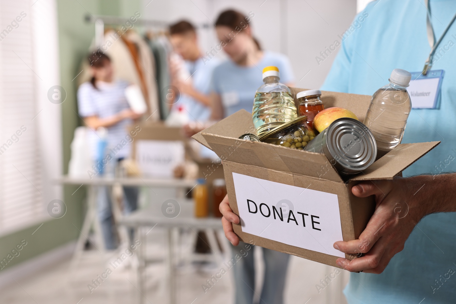 Photo of Volunteer holding donation box with food products indoors, closeup. Space for text