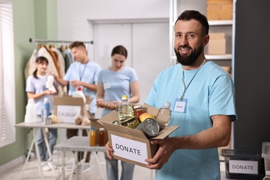 Photo of Volunteer holding donation box with food products indoors, selective focus