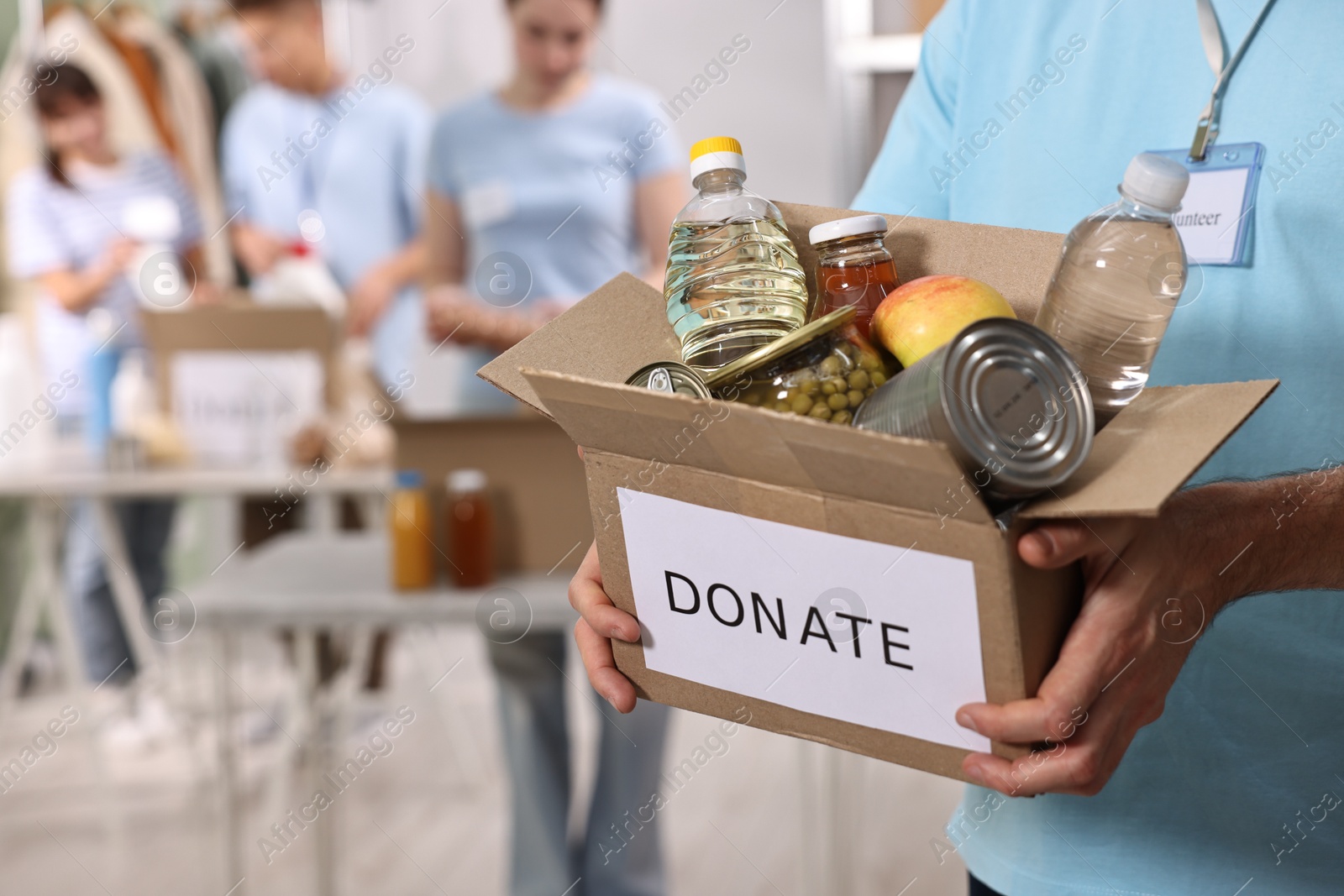 Photo of Volunteer holding donation box with food products indoors, closeup. Space for text