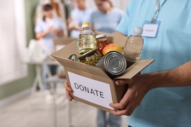 Photo of Volunteer holding donation box with food products indoors, closeup. Space for text