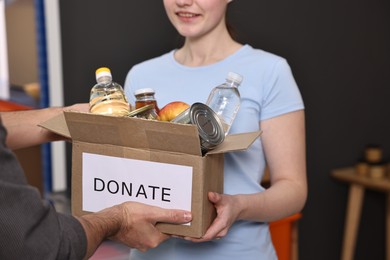 Photo of Volunteers holding donation box with food products indoors, closeup