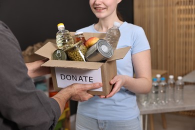 Photo of Volunteers holding donation box with food products indoors, closeup