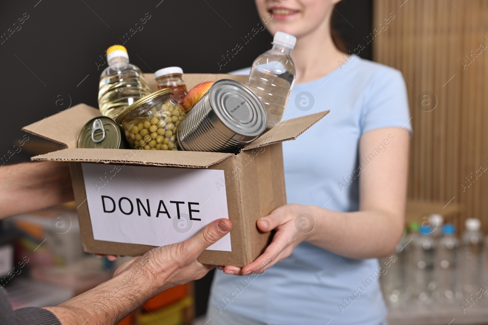 Photo of Volunteers holding donation box with food products indoors, closeup