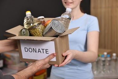 Photo of Volunteers holding donation box with food products indoors, closeup