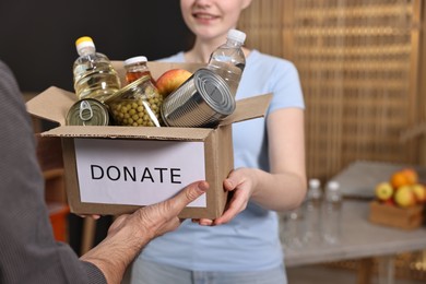 Photo of Volunteers holding donation box with food products indoors, closeup