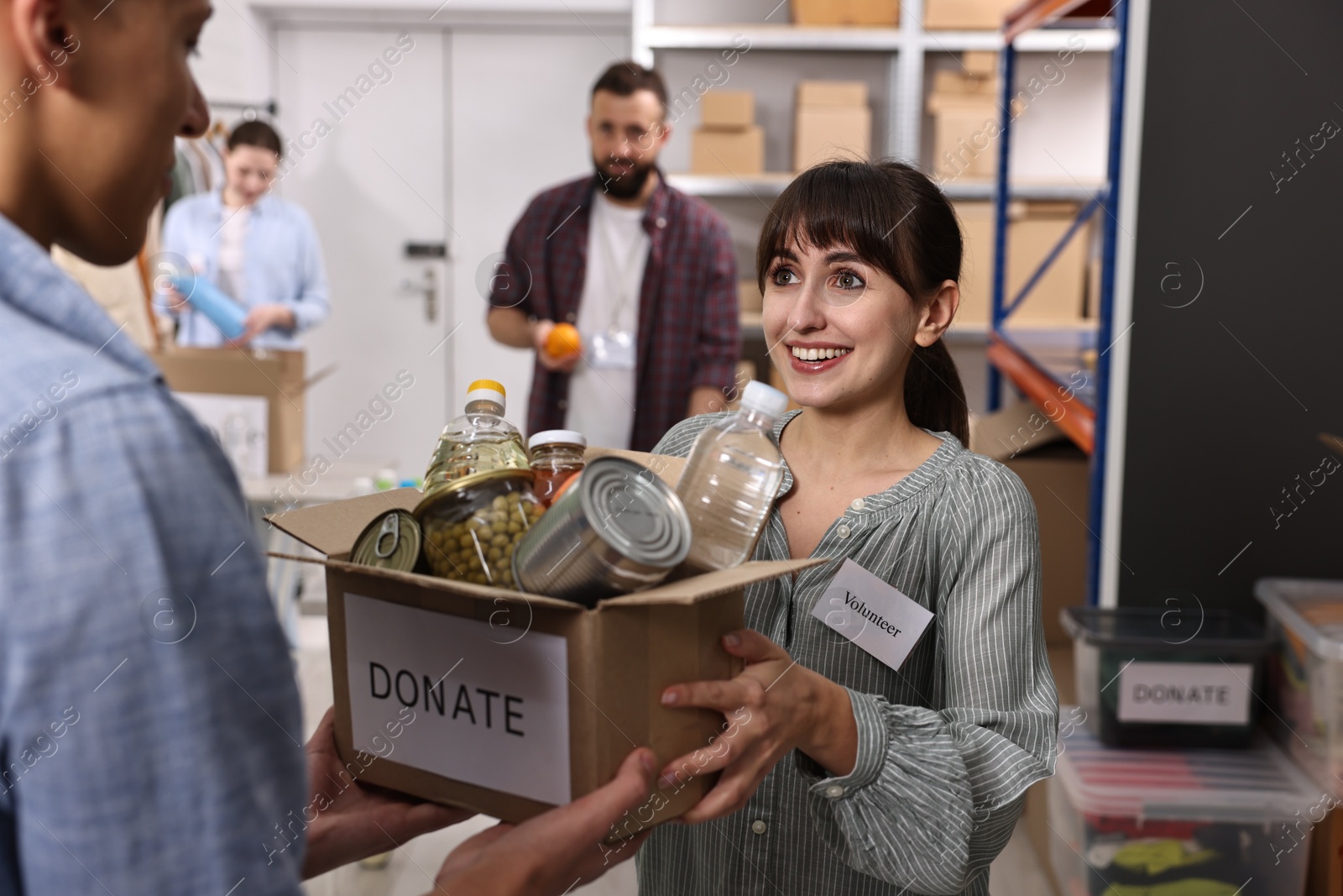 Photo of Volunteers holding donation box with food products indoors, selective focus