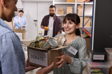 Photo of Volunteers holding donation box with food products indoors, selective focus