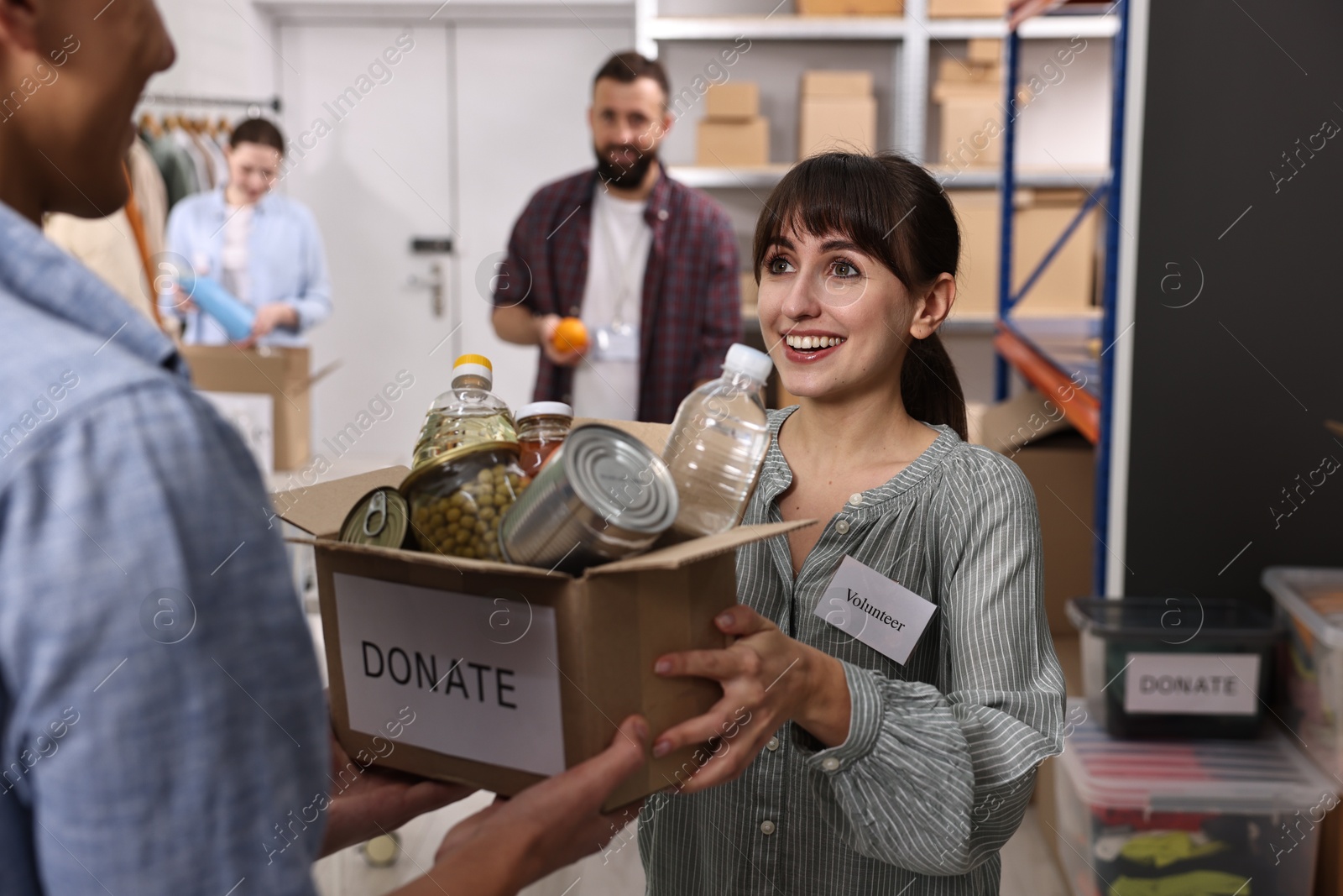 Photo of Volunteers holding donation box with food products indoors, selective focus