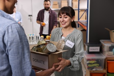 Photo of Volunteers holding donation box with food products indoors, selective focus