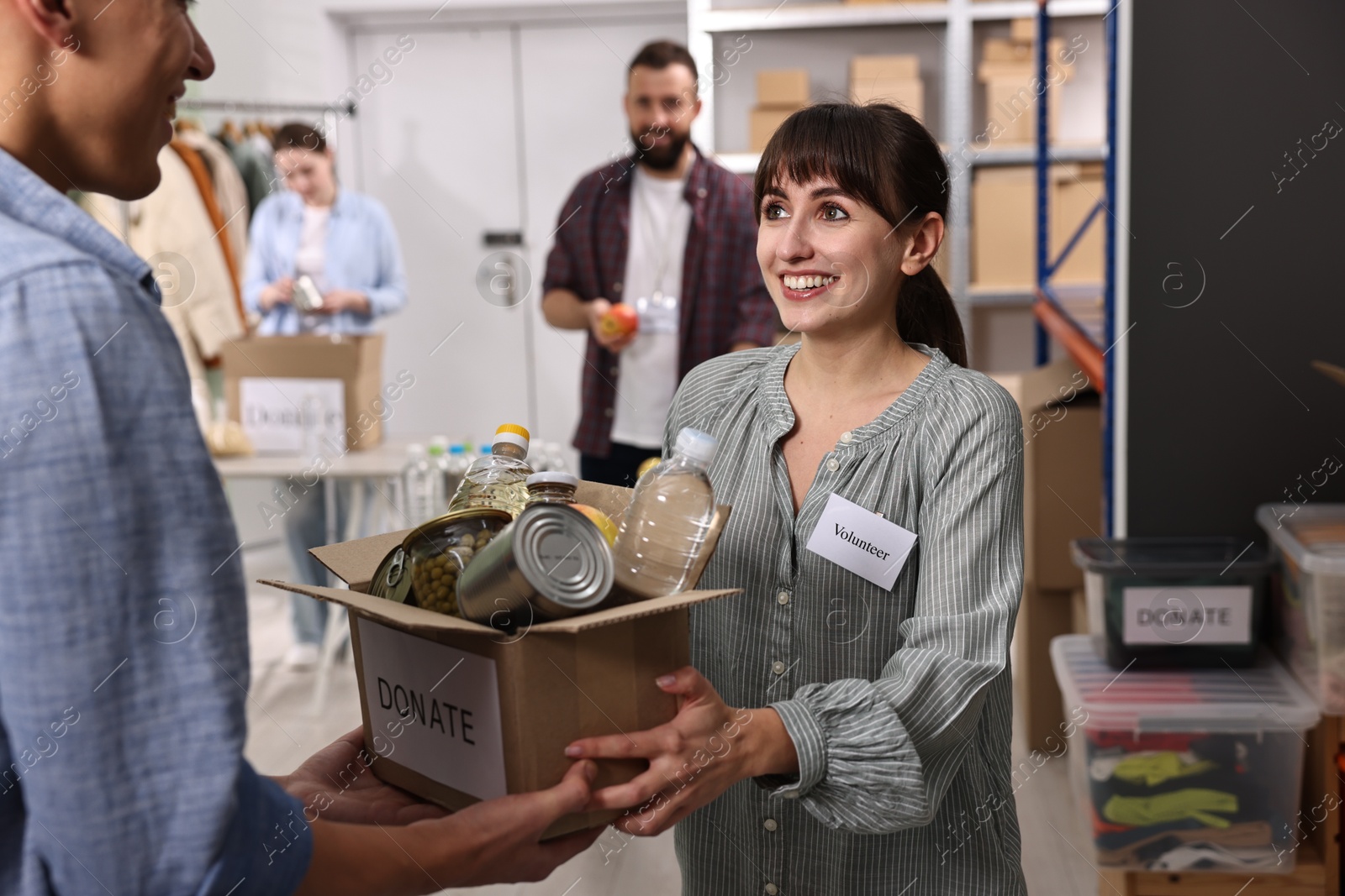 Photo of Volunteers holding donation box with food products indoors, selective focus