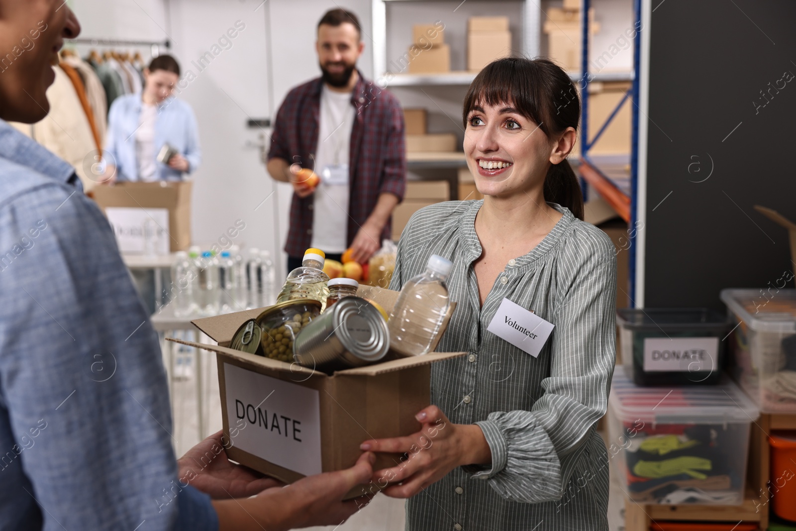 Photo of Volunteers holding donation box with food products indoors, selective focus