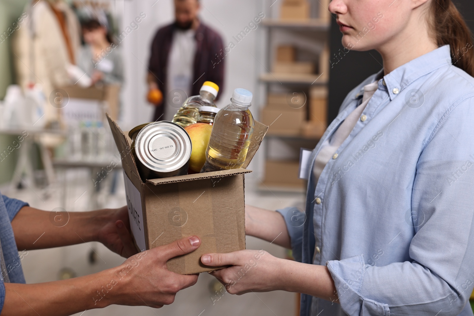 Photo of Volunteers holding donation box with food products indoors, closeup