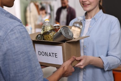 Photo of Volunteers holding donation box with food products indoors, closeup