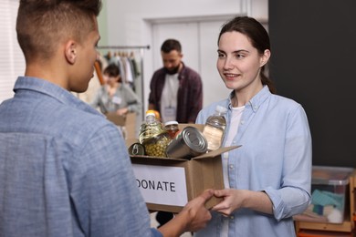 Photo of Volunteers holding donation box with food products indoors, selective focus