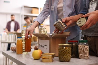 Photo of Volunteers packing food donations at table indoors, closeup