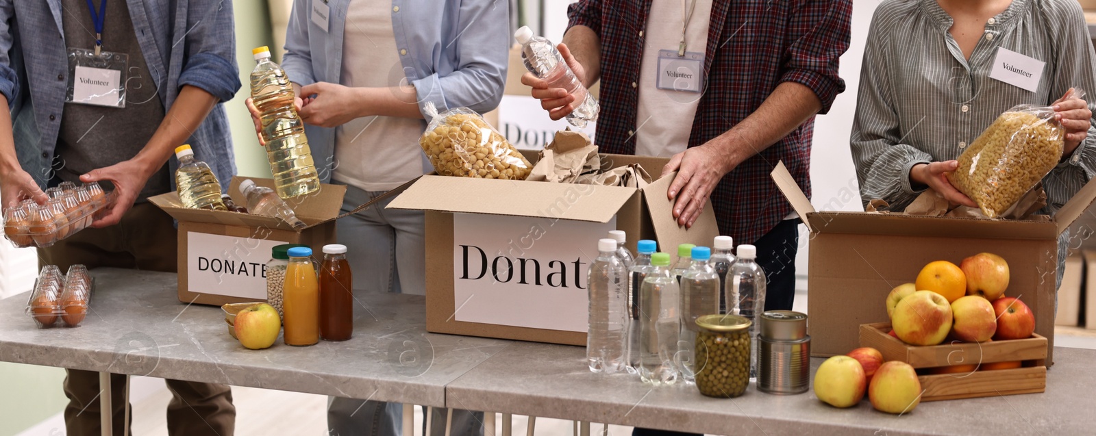 Photo of Group of volunteers packing food donations at table indoors, closeup