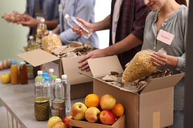 Photo of Group of volunteers packing food donations at table indoors, closeup